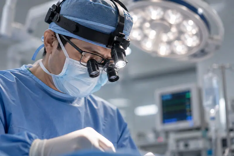 A surgeon wearing a LED headlight and loupes working beneath an overhead LED surgical light